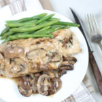 stuffed chicken breast with mushroom cream sauce on white plate, fork and knife to right of plate