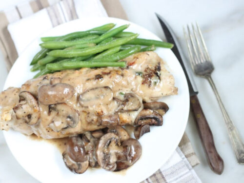 stuffed chicken breast with mushroom cream sauce on white plate, fork and knife to right of plate