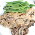 Spinach stuffed chicken with mushroom cream sauce, fresh green beans on white plate.