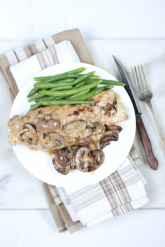 stuffed chicken breast on white plate with mushroom cream sauce, green beans on plate.