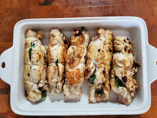 stuffed chicken breasts in white rectangle baking dish on butcher block