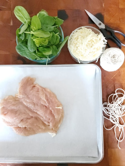 stuffed chicken breasts being made on butcher block, spinach and mozzarella in clear glass bowls