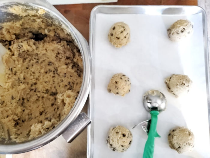 chocolate chip cookie dough scooped out with ice cream scoop on half sheet pan lined with parchment paper.