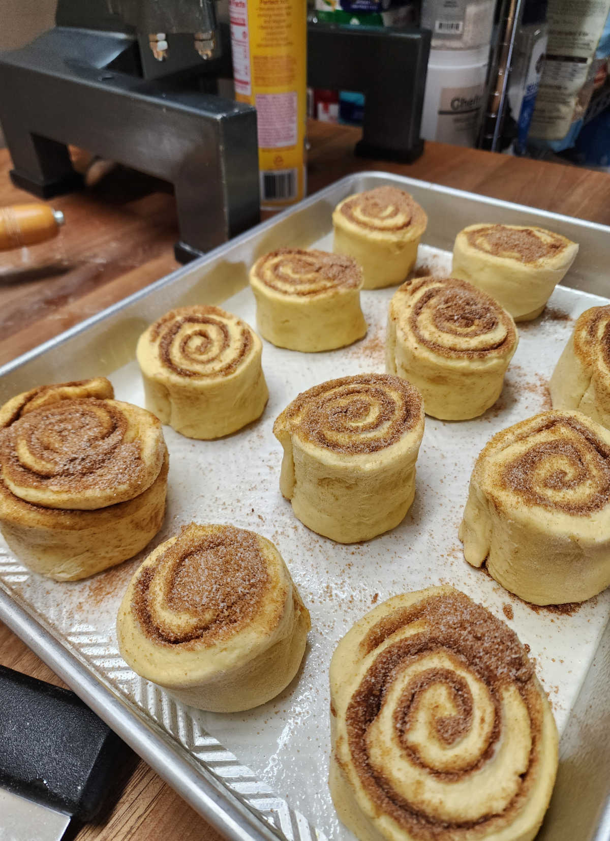 Unbaked cinnamon rolls in high sided half sheet pan on butcher block.
