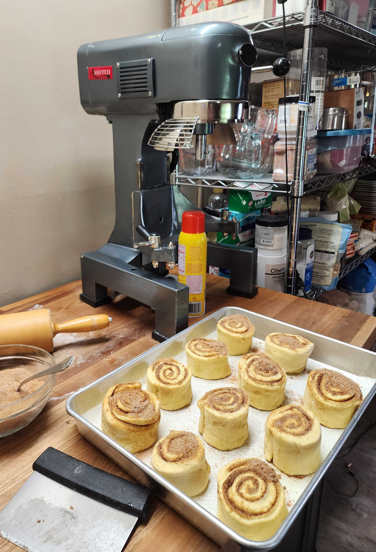 Cinnamon rolls in baking pan on butcher block, big stand mixer in background.