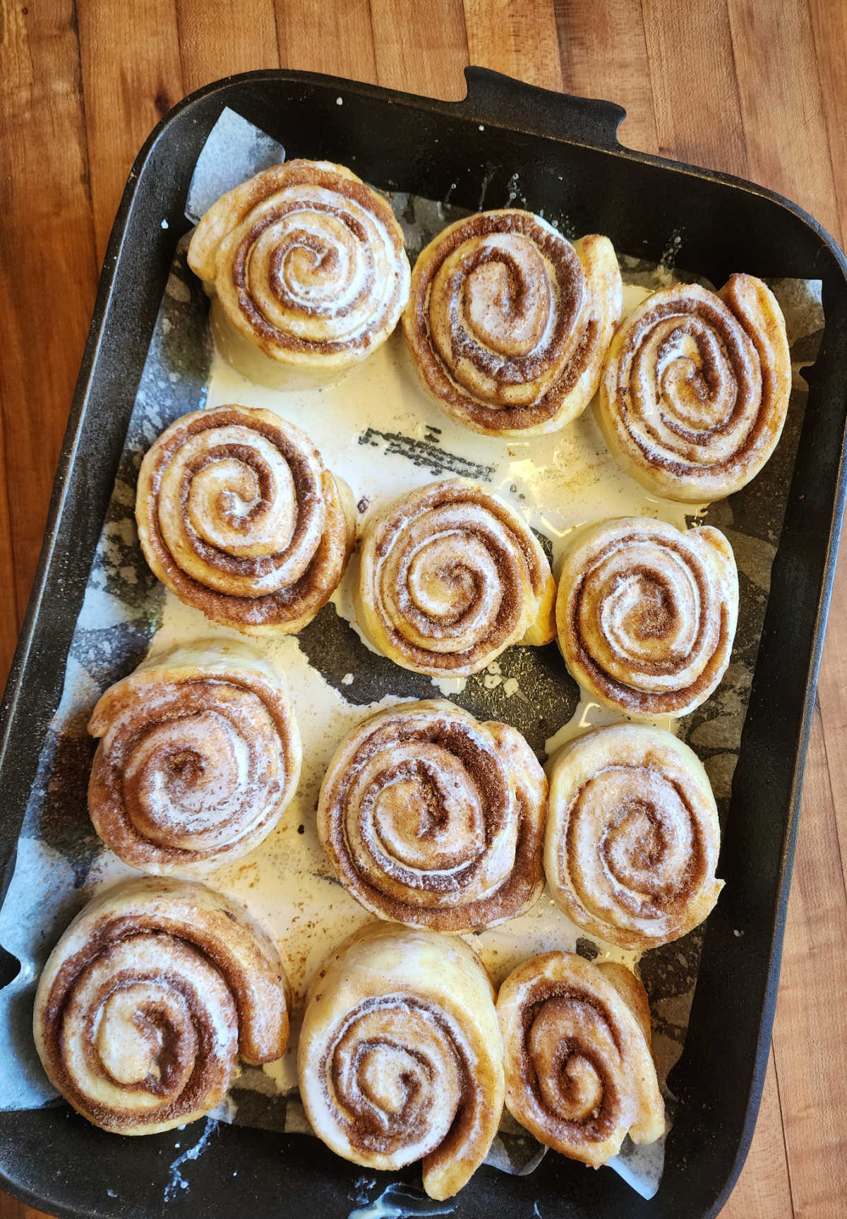Unbaked cinnamon rolls brushed with heavy cream in cast iron cake pan.