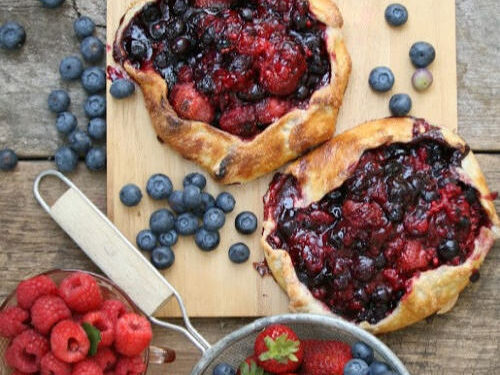 mixed berry galettes on reclaimed wood boards, berries in metal strainer with wooden handle