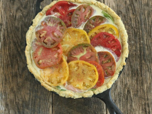 quiche in cast iron skillet with multi colored heirloom tomato slices on top