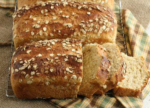 loaves of oat bread on baking rack, one loaf sliced
