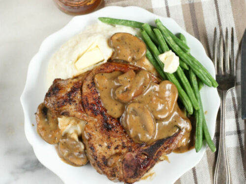 pork chops with mushroom gravy on white plate with fresh green beans and mashed potatoes
