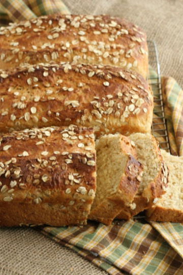 three loaves of homemade bread cooling on baking rack, front loaf sliced