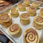 Unbaked cinnamon rolls in metal baking pan on butcher block.