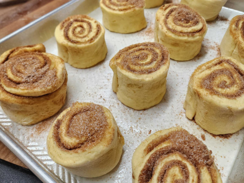 Unbaked cinnamon rolls in metal baking pan on butcher block.