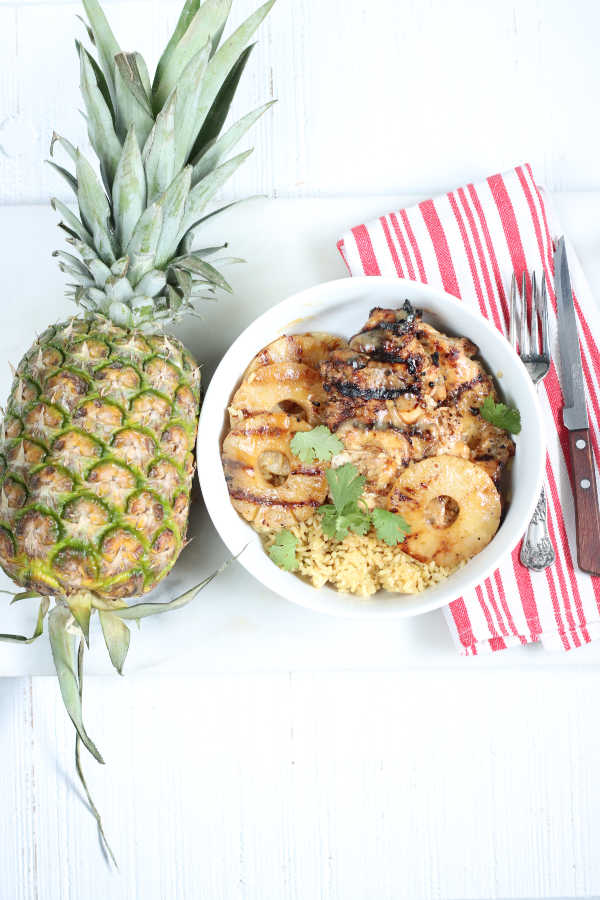 white bowl of brown rice and grilled chicken. Whole pineapple to the left of bowl