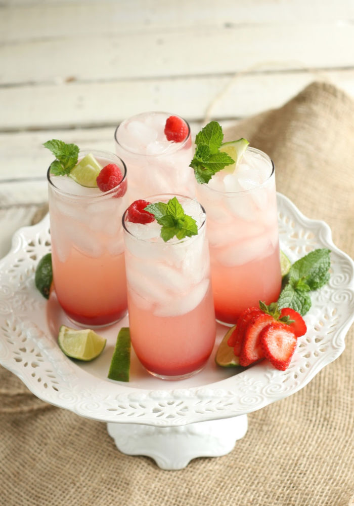glasses of strawberry spiked lemonade on white ceramic footed cake dish