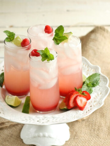 Strawberry cocktails in clear cylinder glasses with ice cubes, topped with fresh mint and sliced strawberries