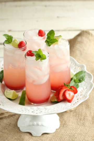Strawberry cocktails in clear cylinder glasses with ice cubes, topped with fresh mint and sliced strawberries