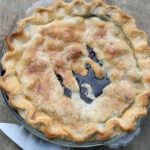 Blueberry pie in clear glass pie dish on reclaimed wood.
