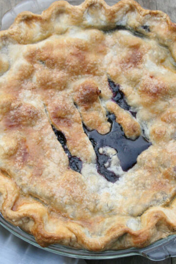 Blueberry pie in clear glass pie dish on reclaimed wood.