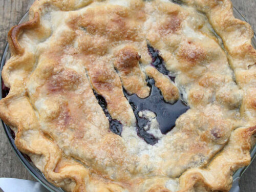 Blueberry pie in clear glass pie dish on reclaimed wood.