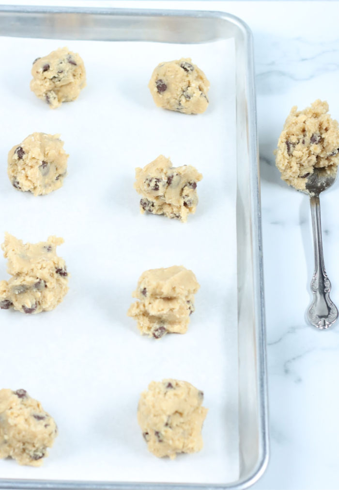 chocolate chip cookie dough on half sheet pan lined with white parchment paper, table spoon with cookie dough to right