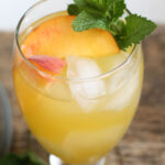 Glass of white sangria with peaches, ice cubes and sprig of fresh mint.