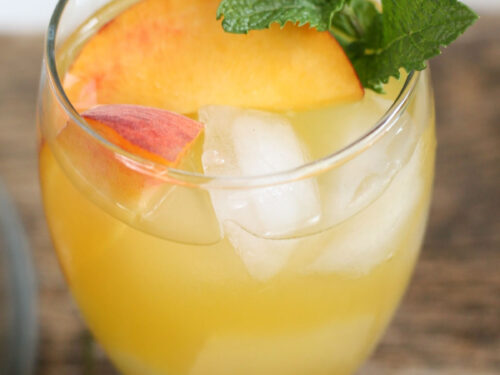 Glass of white sangria with peaches, ice cubes and sprig of fresh mint.