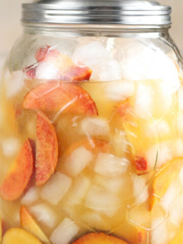 Drink dispenser with white sangria, peach slices, ice cubes.