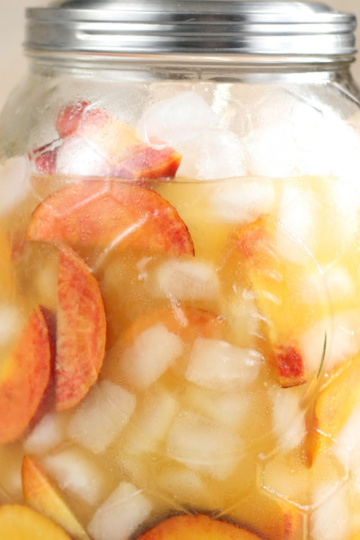 Drink dispenser with white sangria, peach slices, ice cubes.