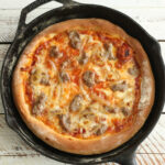 Pizza in a cast iron skillet with golden crust and cheese.