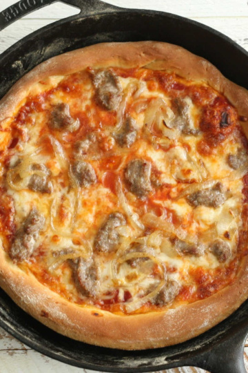 Pizza in a cast iron skillet with golden crust and cheese.