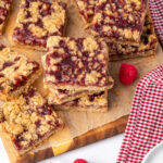 Raspberry bars cut into squares on wood cutting board.