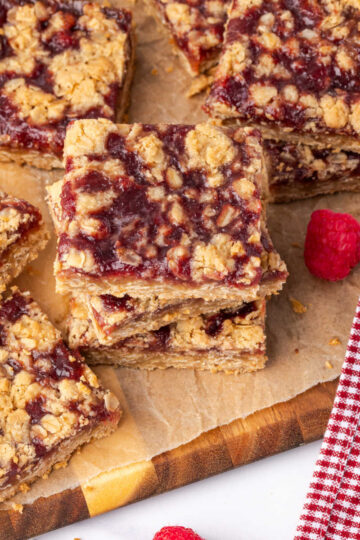 Raspberry bars cut into squares on wood cutting board.