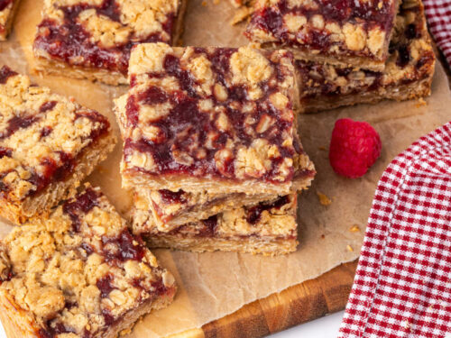 Raspberry bars cut into squares on wood cutting board.