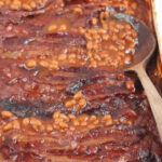 Baked beans in white rectangle baking dish, wooden spoon in dish on right.