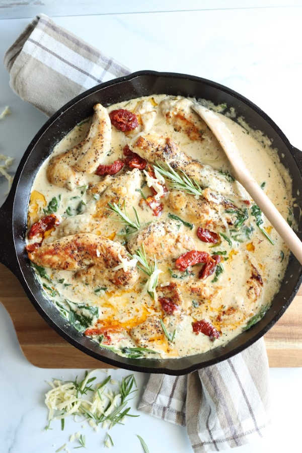 cast iron skillet with chicken, spinach, sun dried tomatoes, and cream sauce