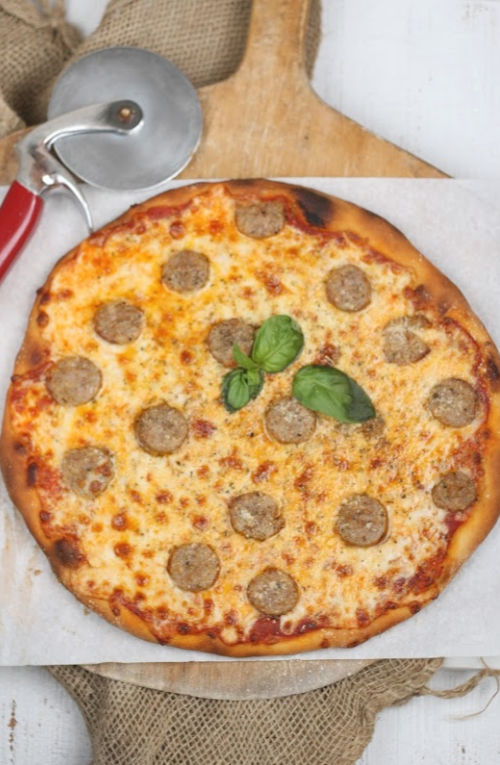Italian style pizza with sliced sausage links on top, browned cheese, topped with fresh basil leaf.