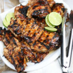 Grilled chicken on white oval serving plate with metal tongs.