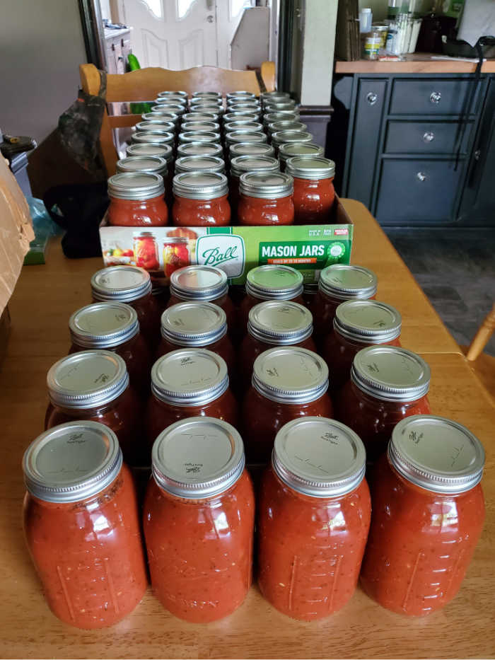 Quart and pint glass Mason jars with homemade pasta sauce, stacked on kitchen table.