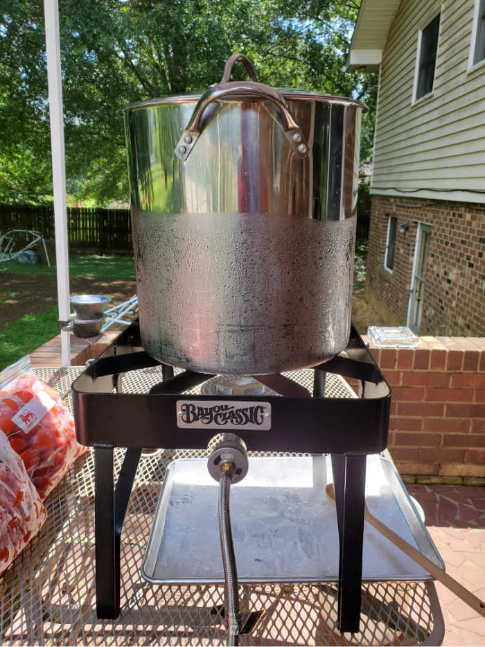 Outdoor burner with large stockpot on patio table. Bags of tomatoes to left.