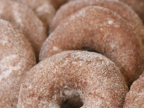 Apple cider donuts lined up against each other on half sheet pan lined with white parchment paper