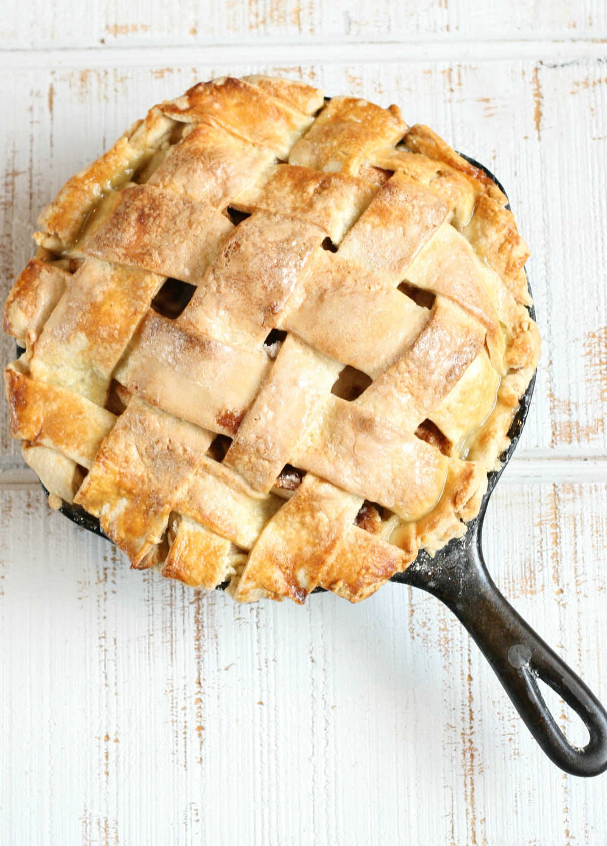 Apple Pie with lattice crust in a small cast iron skillet on white reclaimed wood.