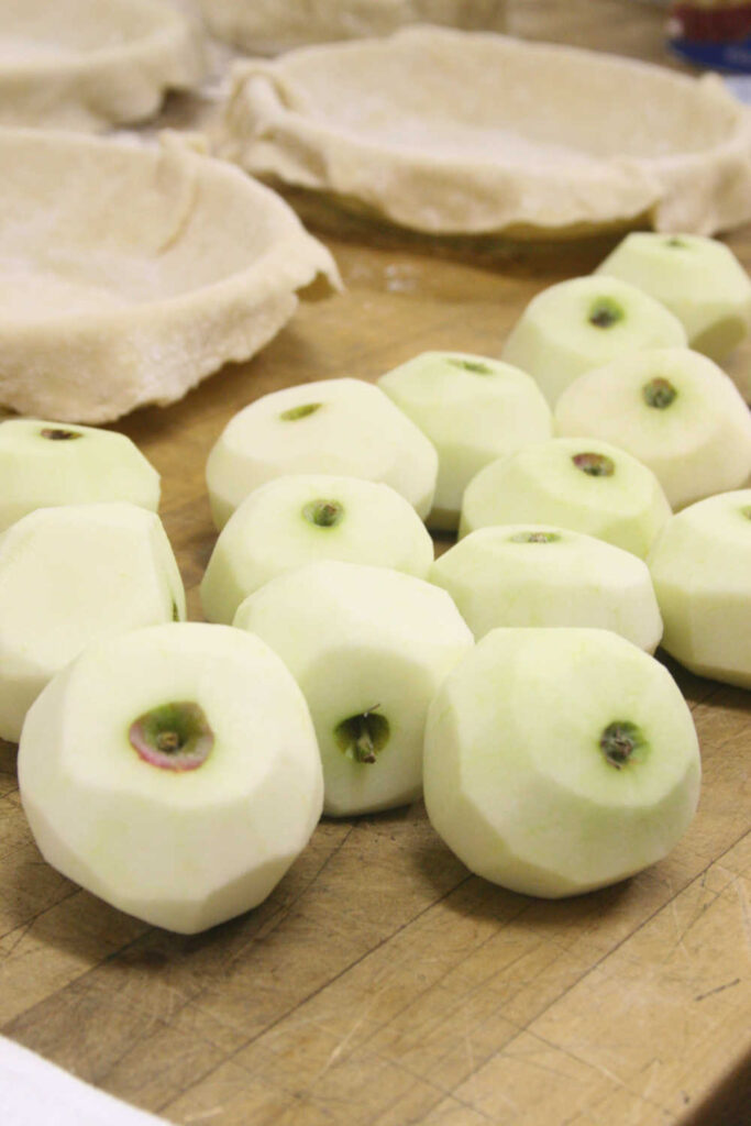 peeled apples on wooden butcher block, unbaked pie shells in background