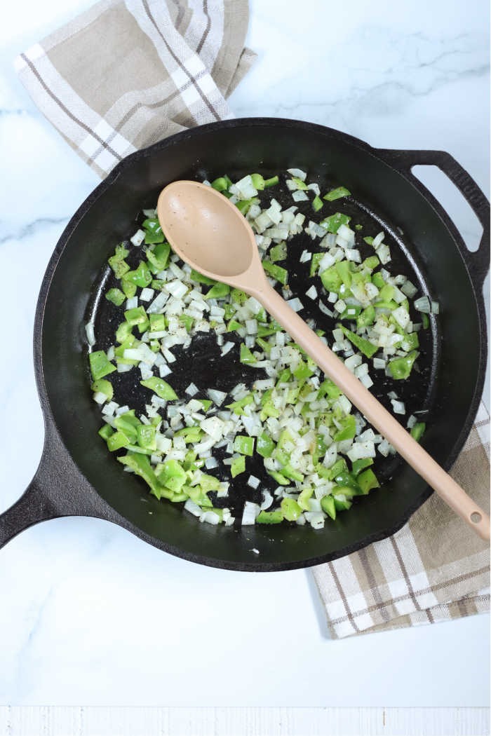large cast iron skillet with chopped onion and green bell pepper. Spoon in the pan.