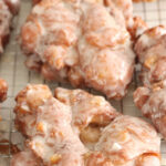 Apple fritters with glaze on baking rack.
