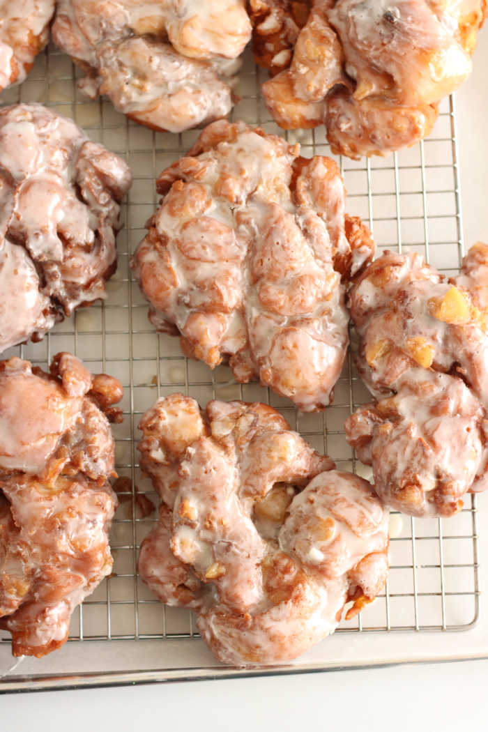 apple fritter donuts on a half sheet pan and baking rack dripping dry with glaze.