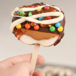 Holding caramel apple slice with chocolate.