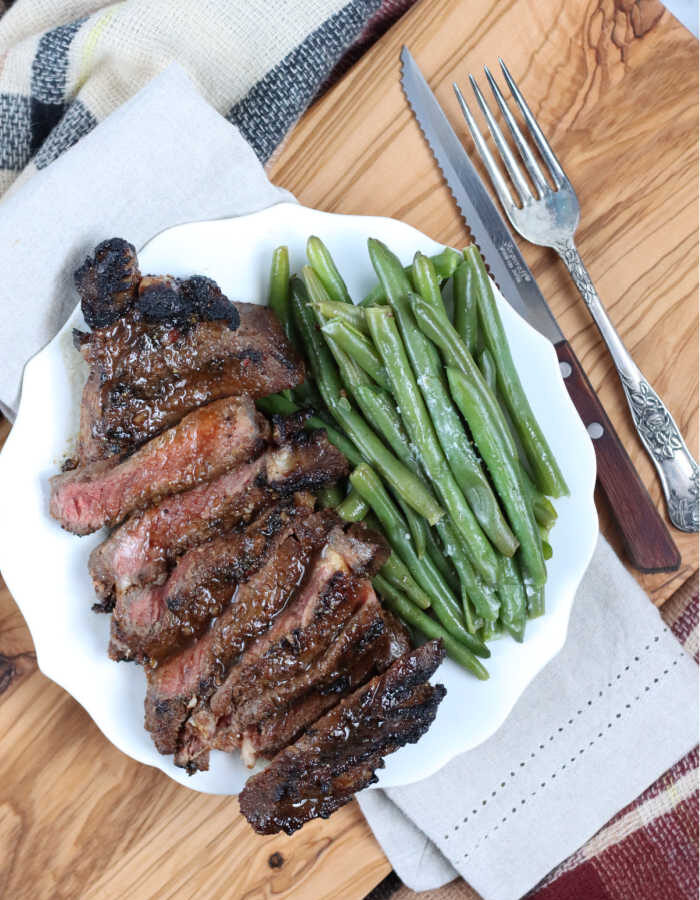 sliced grilled ribeye steak on small white plate, fresh green beans to side