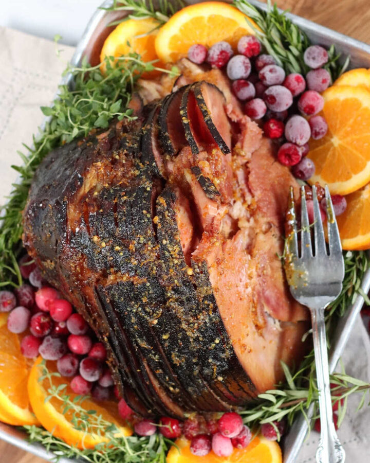 Spiral sliced ham in roasting pan with orange slices and frozen cranberries.