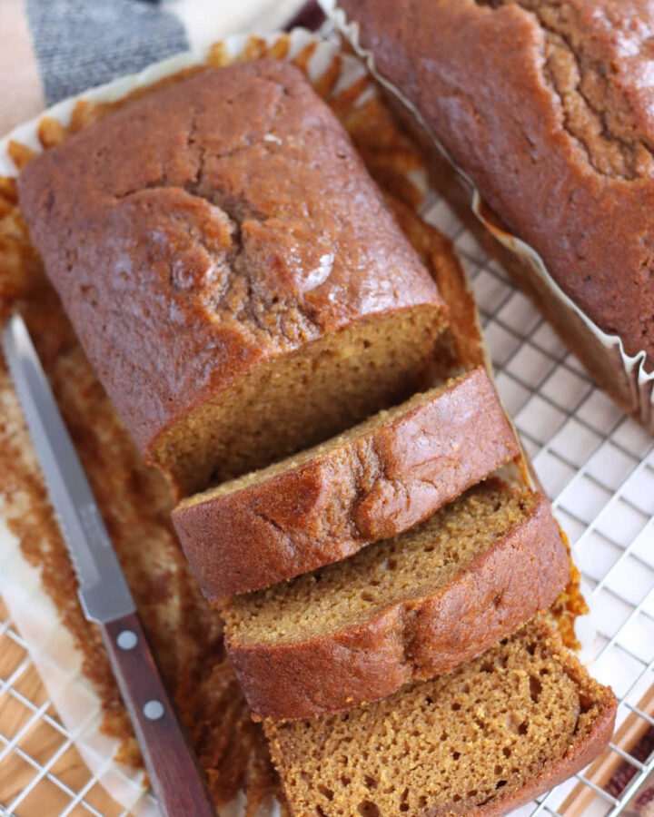 loaves of pumpkin bread on wooden cutting board, one partially sliced.